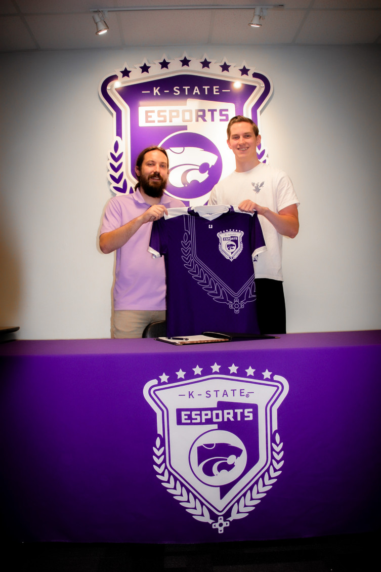 2 men standing in front of the esports logo holding up an esports jersey