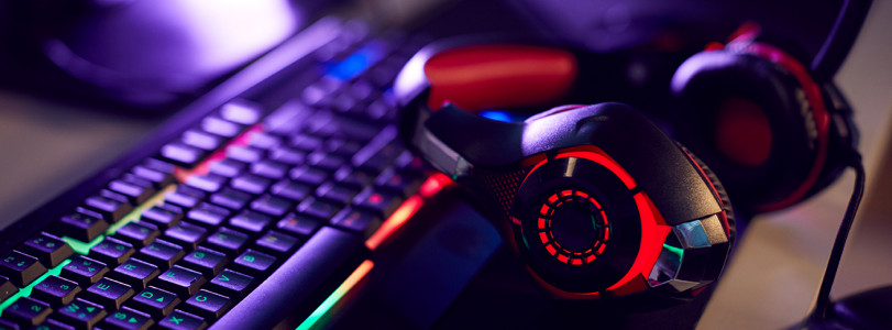 red and black gaming headset next to keyboard with multicolored lighting